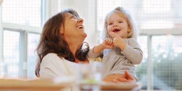 Mature new mother with her toddler laughing in the kitchen happily 