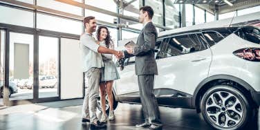 couple shaking hands with car salesman next to SUV