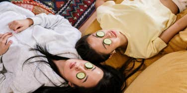 two people laying side by side with cucumbers on their eyes