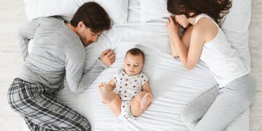 couple sleeping in bed with baby between them